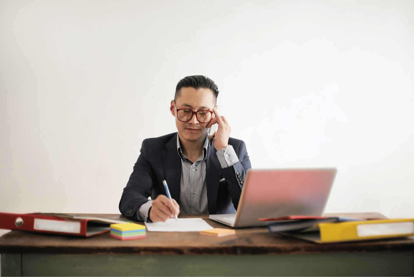 Man at desktop, talking on phone and taking notes