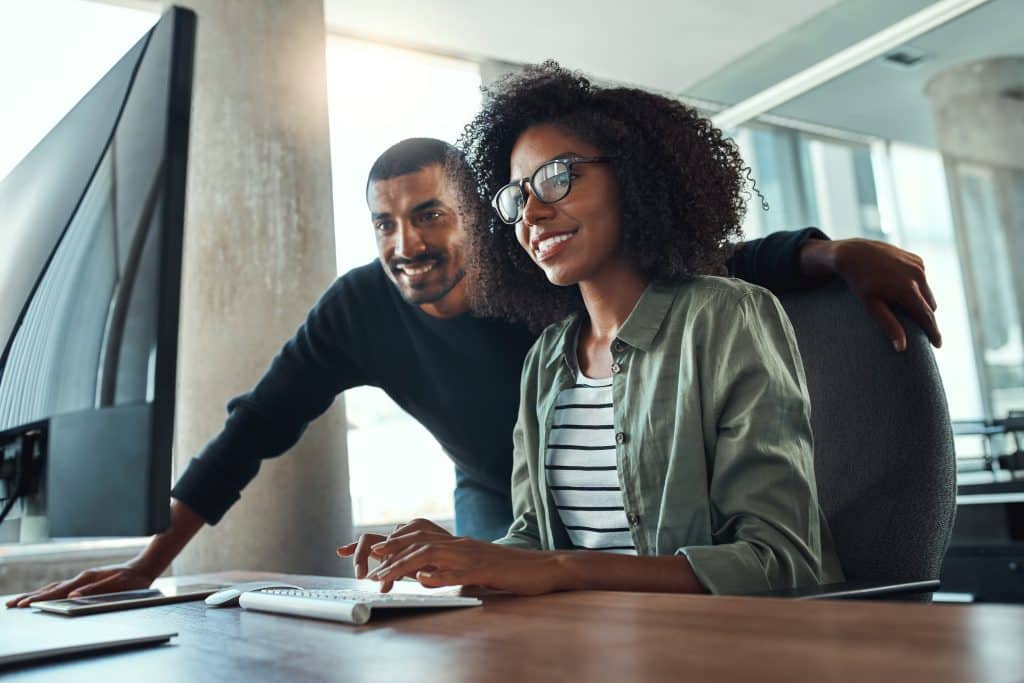 A man looks over the shoulder of a femal coworker as they look at procure-to-pay solutions.