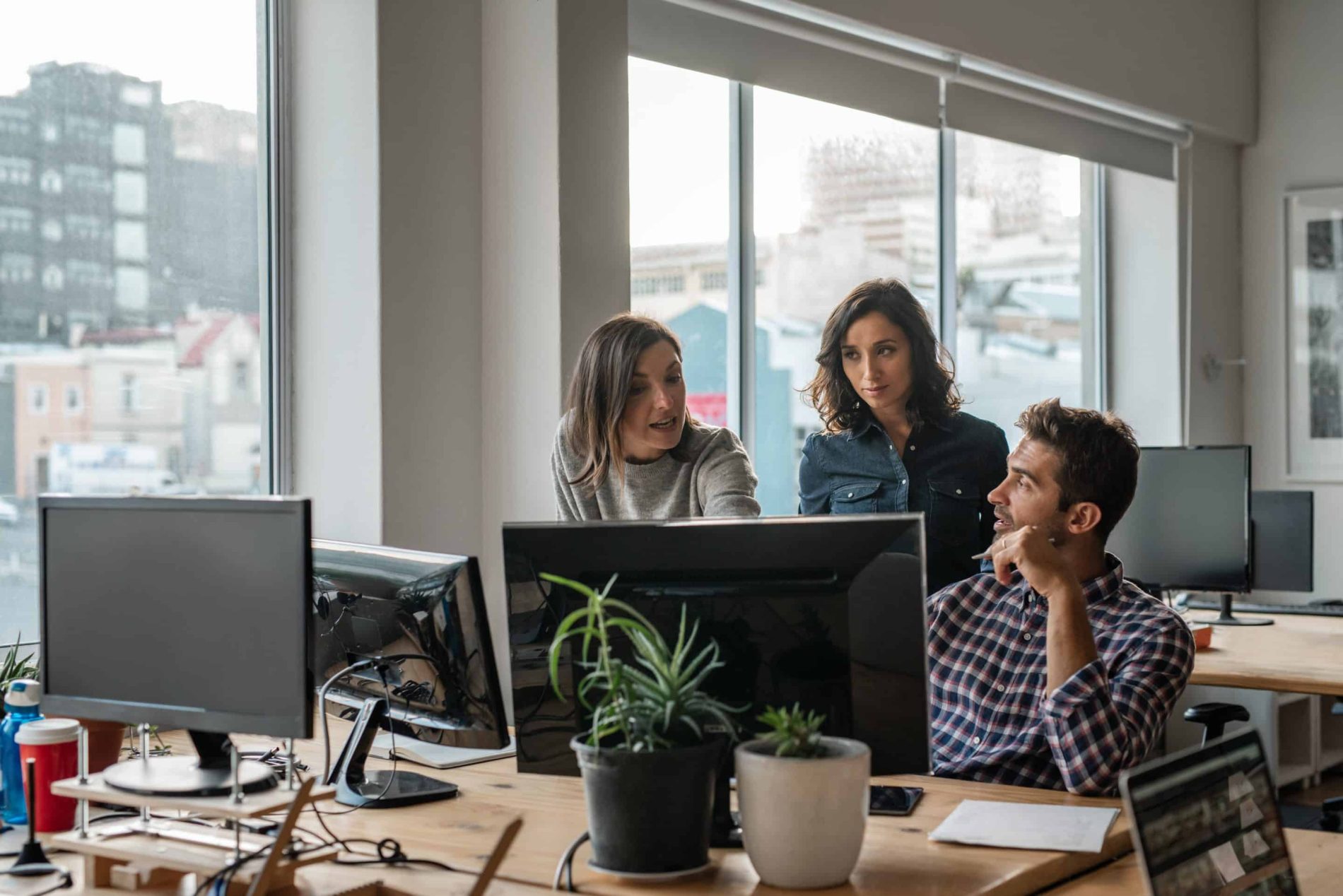 Three employees look for solutions to improve their AP process on a computer in a large office.