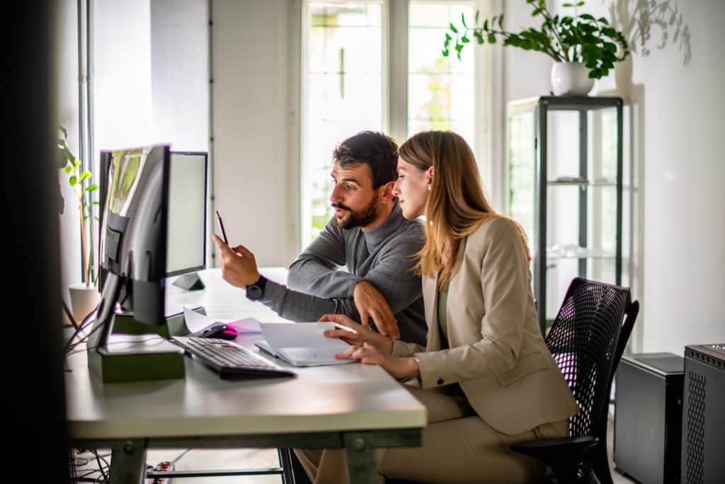 A male coworker shows female coworker how to use new procurement software to improve user adoption.