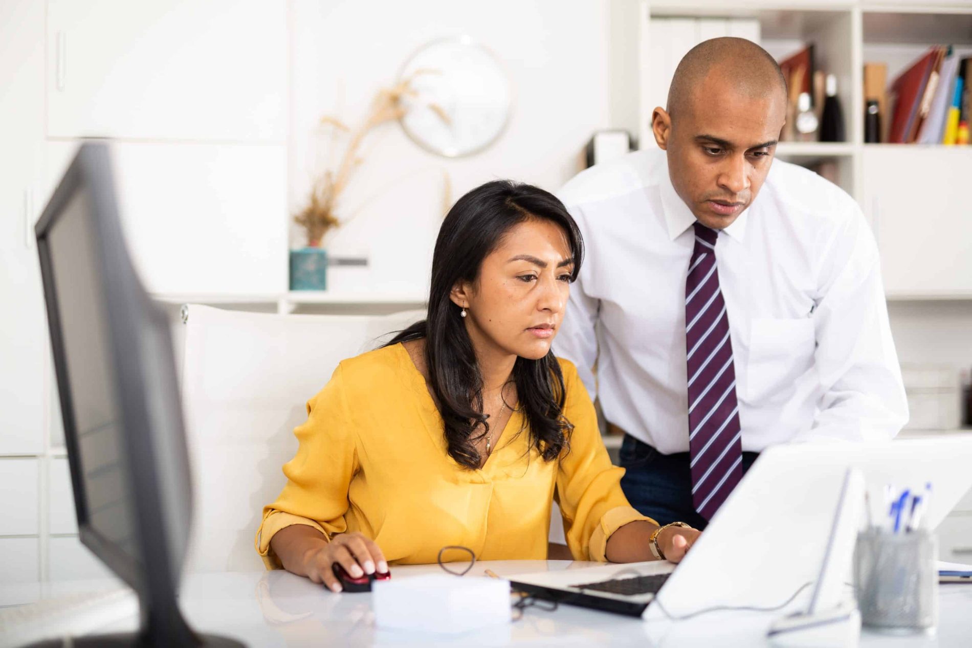 Focused male and female business colleagues looking at laptop screen, discussing new project in office.