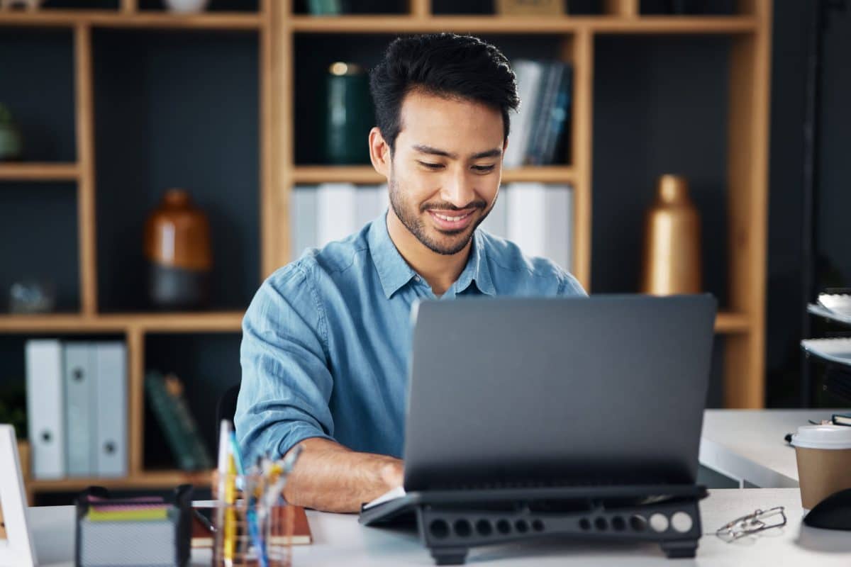 A young, smiling businessman working on his laptop in an office.