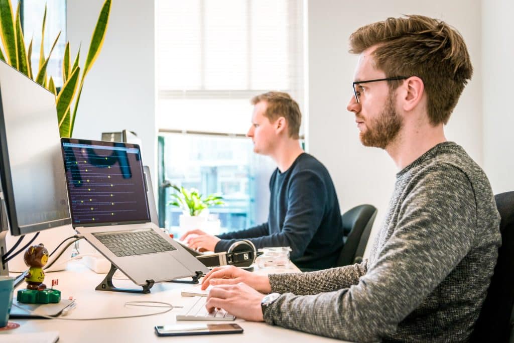 Two employees sitting at an office desk and using e-procurement on their computers to automate tasks.